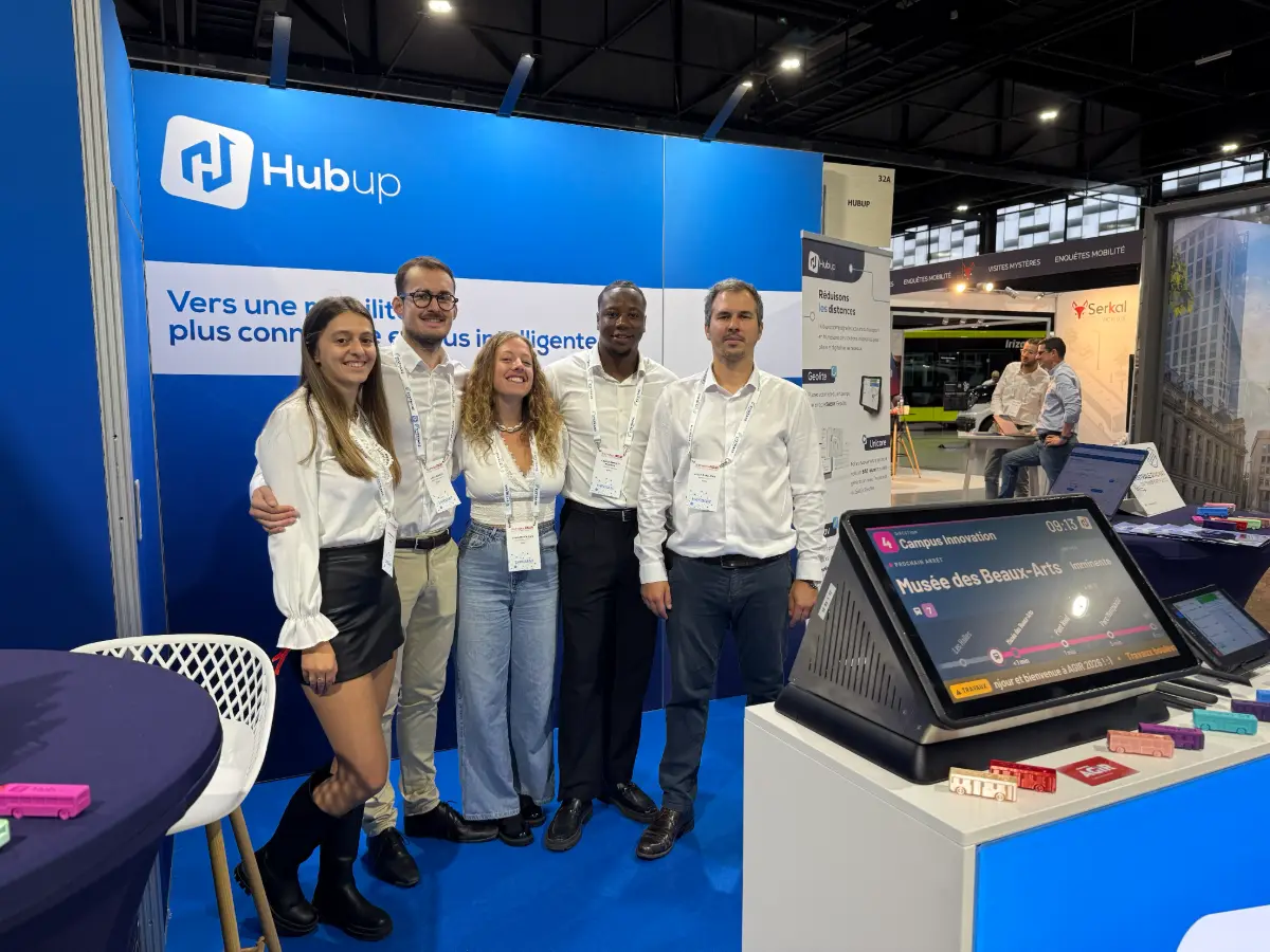 Une partie de l’équipe Hubup sur le stand Hubup, devant un écran d’information voyageur